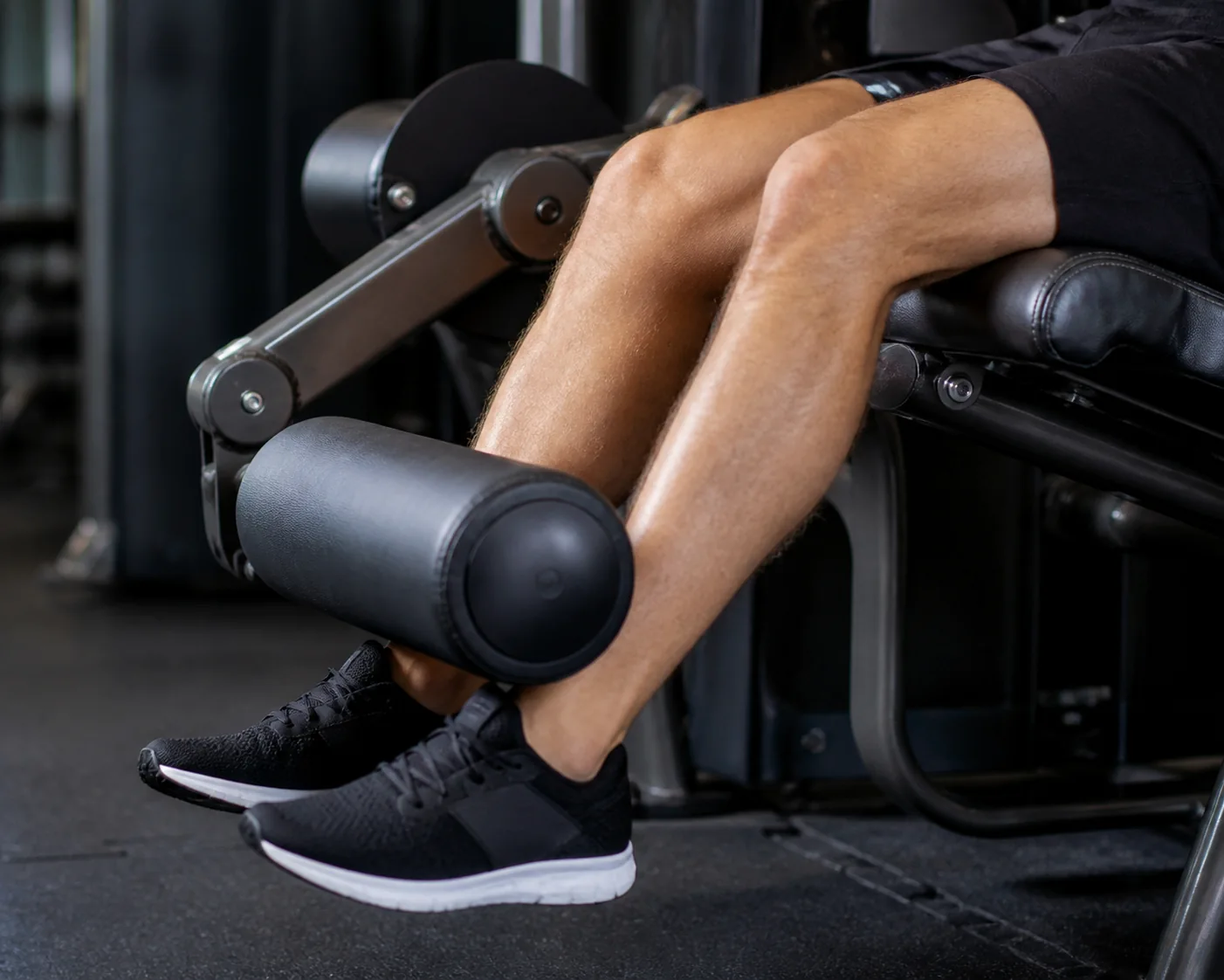 Leg-extension roller contacting the front of the lower shins above the ankles