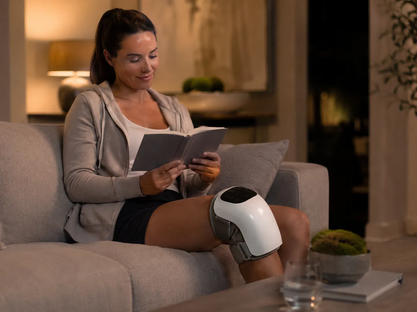 Woman relaxing on a sofa while using the FlexiKnee knee massager in the evening